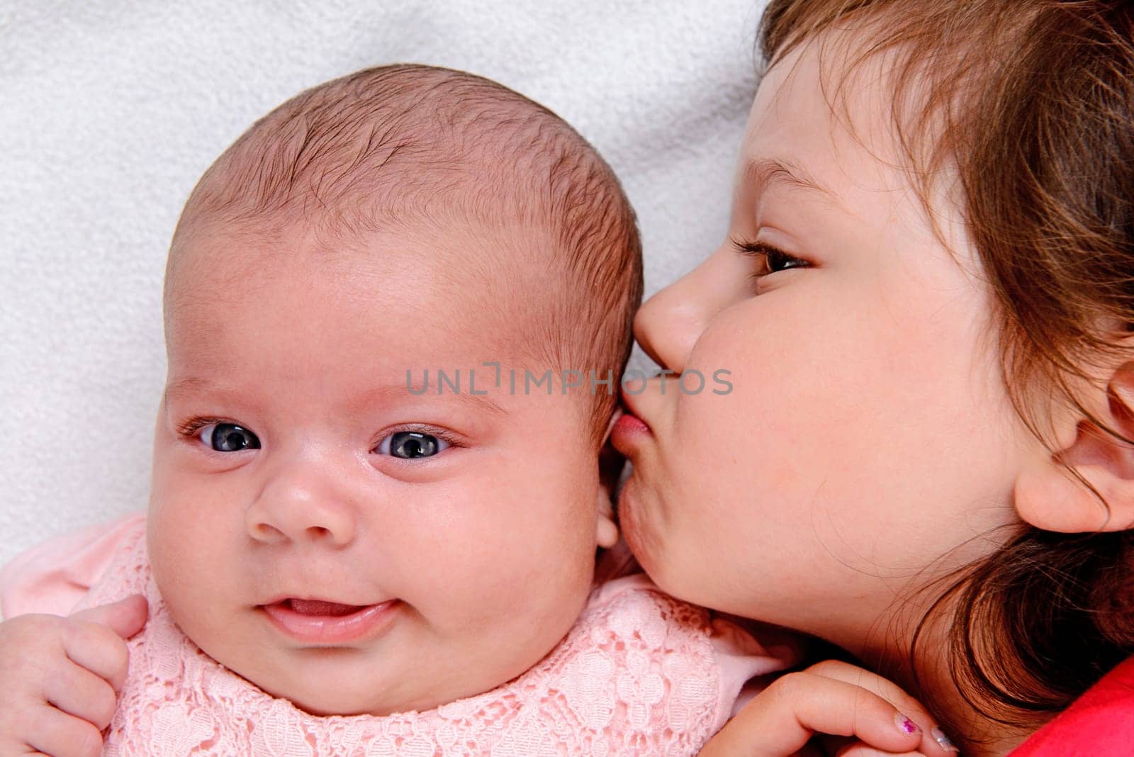 little girl kissing her baby- sister in front of white background