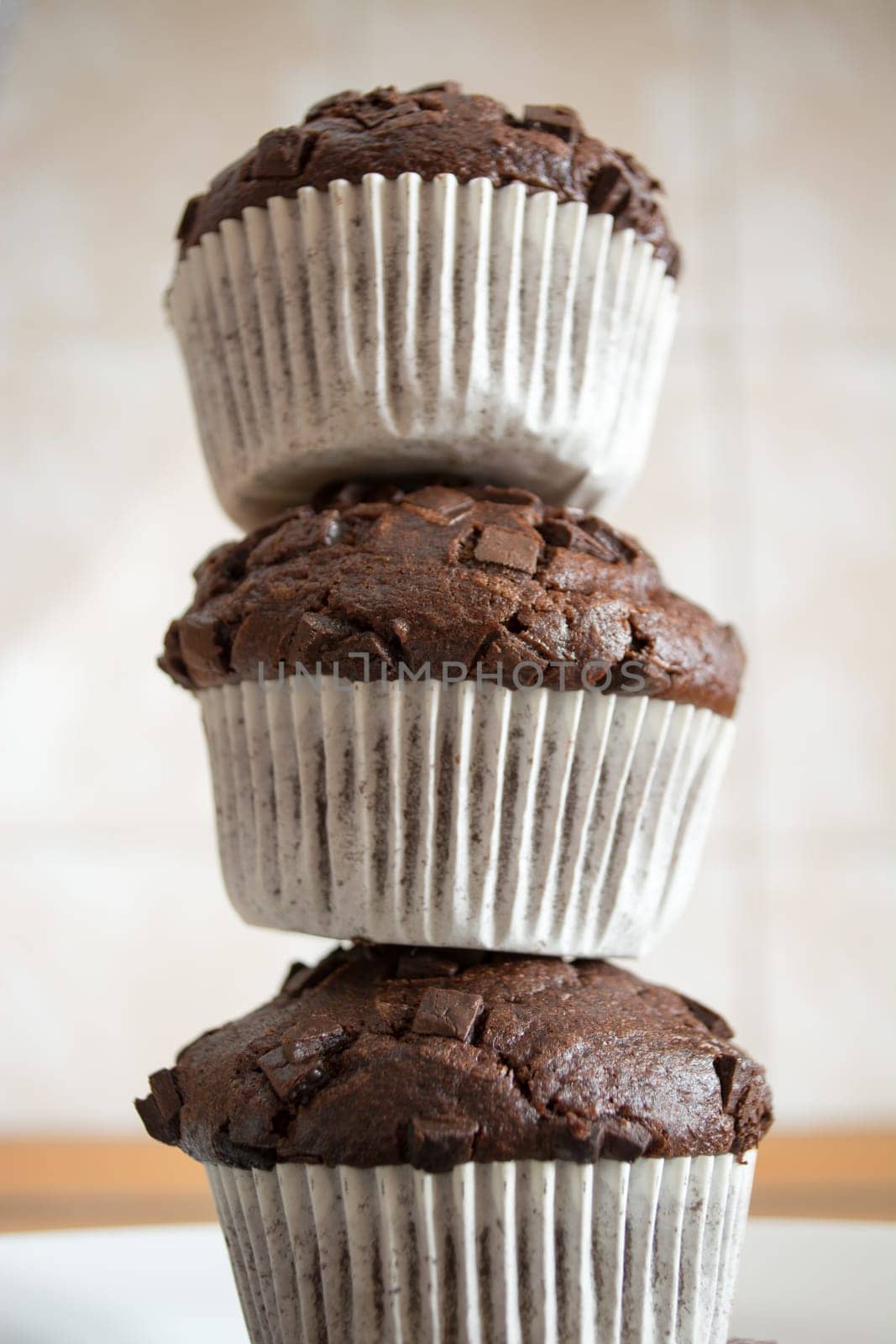 Three chocolate cupcakes stacked to form a tower in the kitchen
