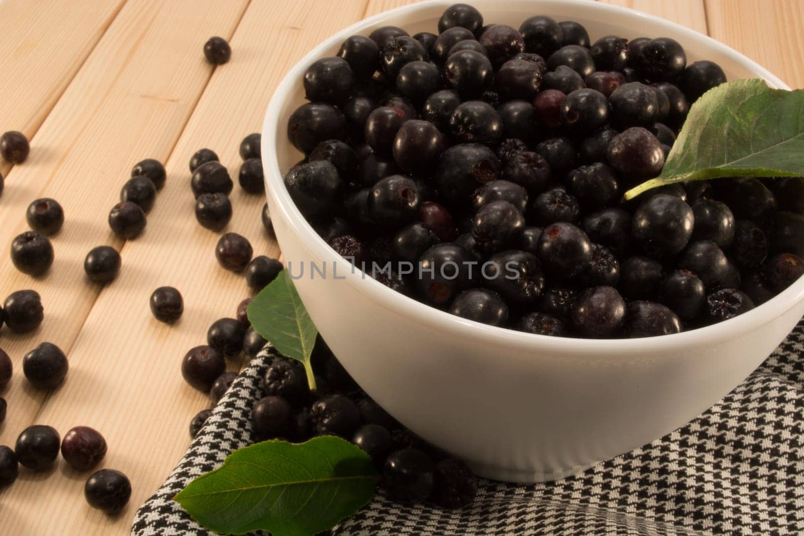 White bowl full with fresh and tasty aronia spilled on wooden table