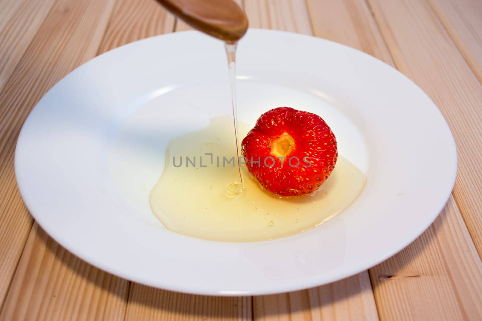 Honey dripping from wooden spoon on straberry