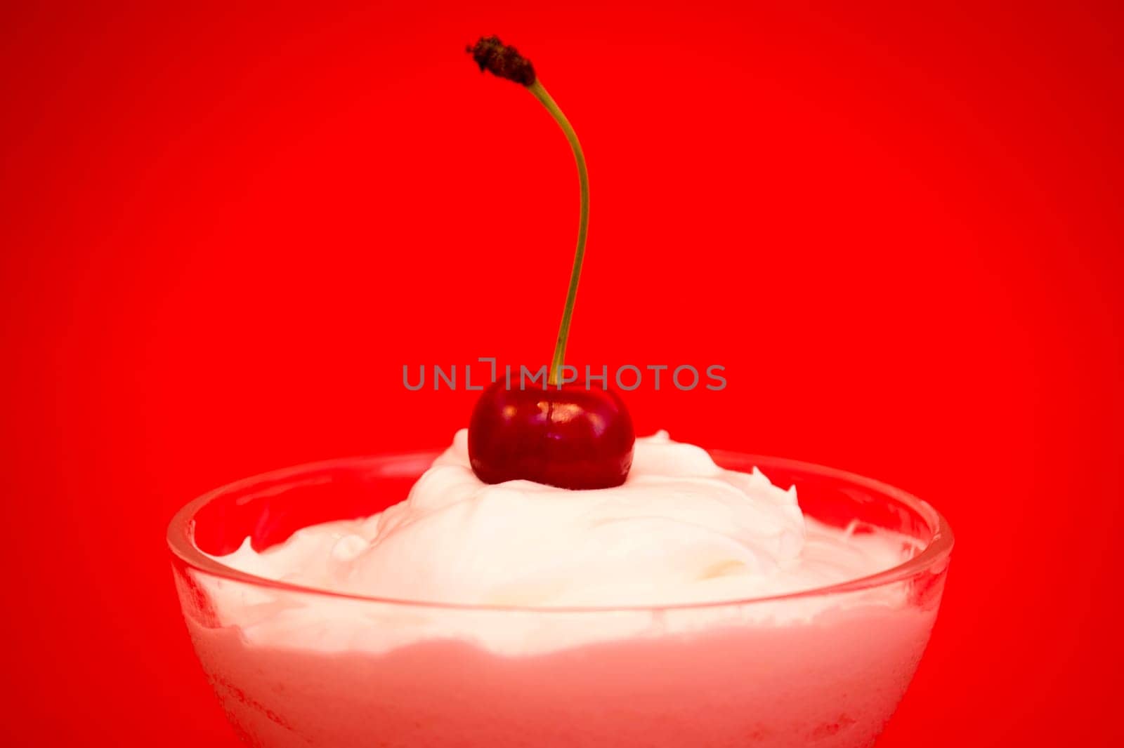 Vanilla cream with cherry on top in a glass cup on red background