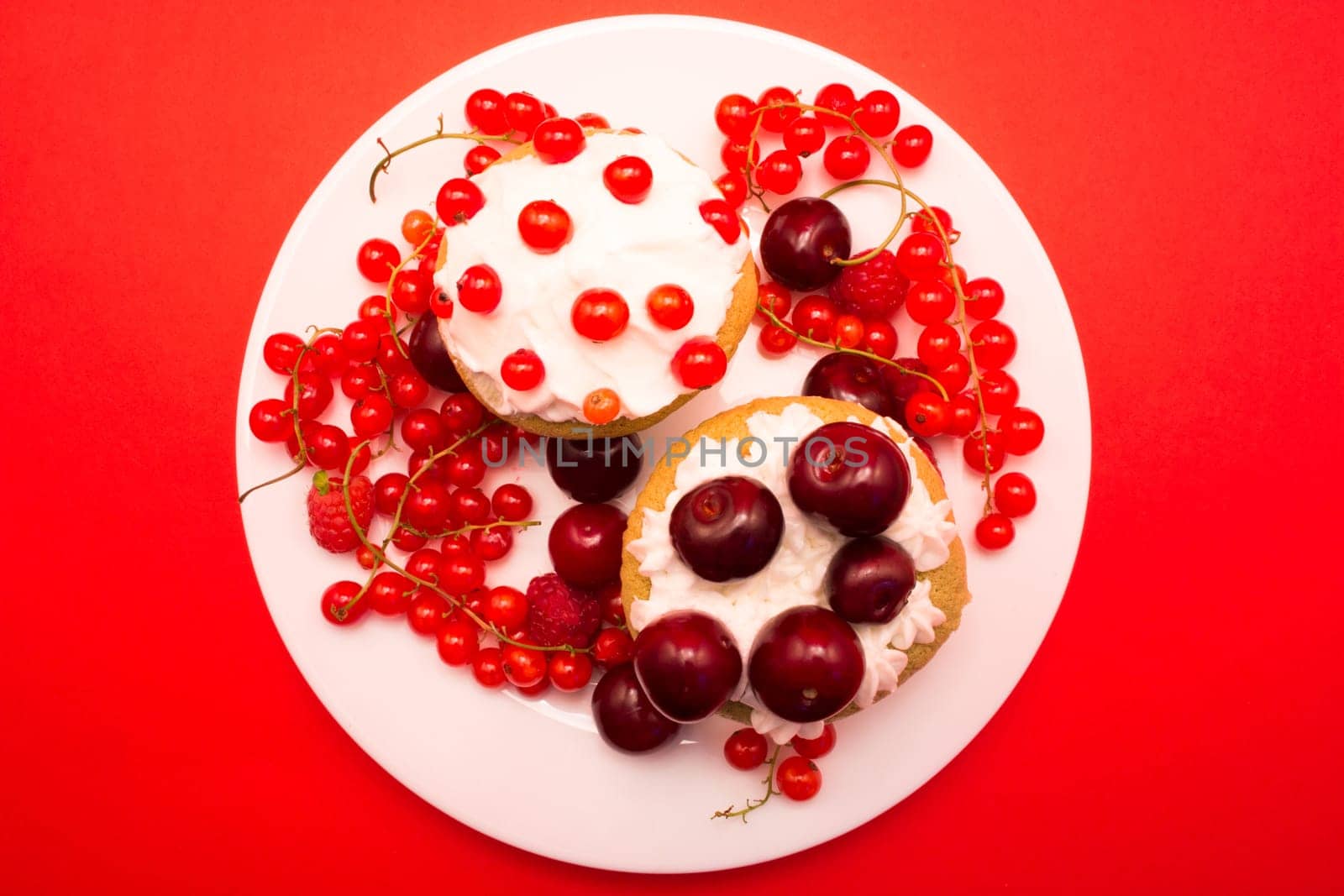 Cupcakes with cherries and currant shoot from upper angle on red background