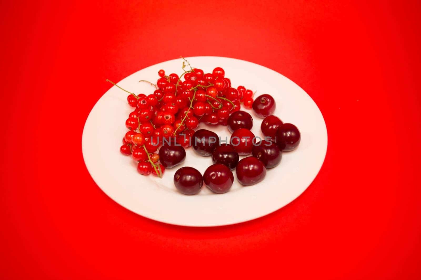 White plate with cherries and red currant on red background
