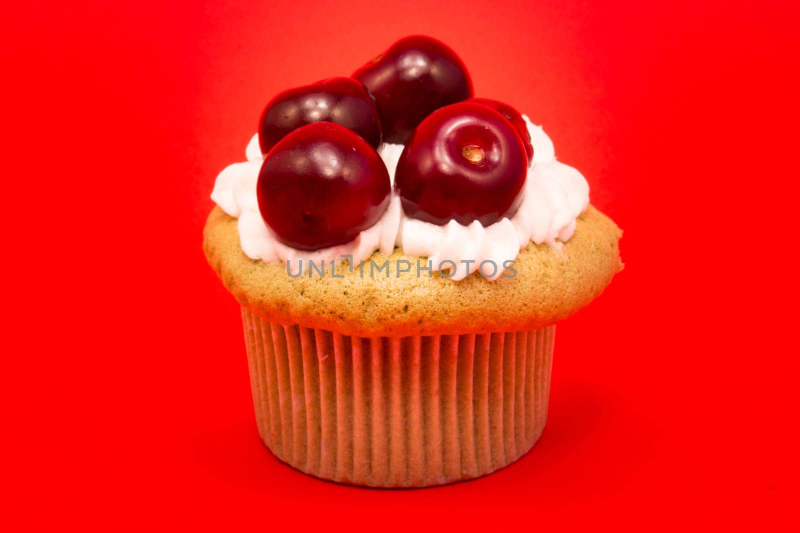 Cupcake with cherries isolated on red background