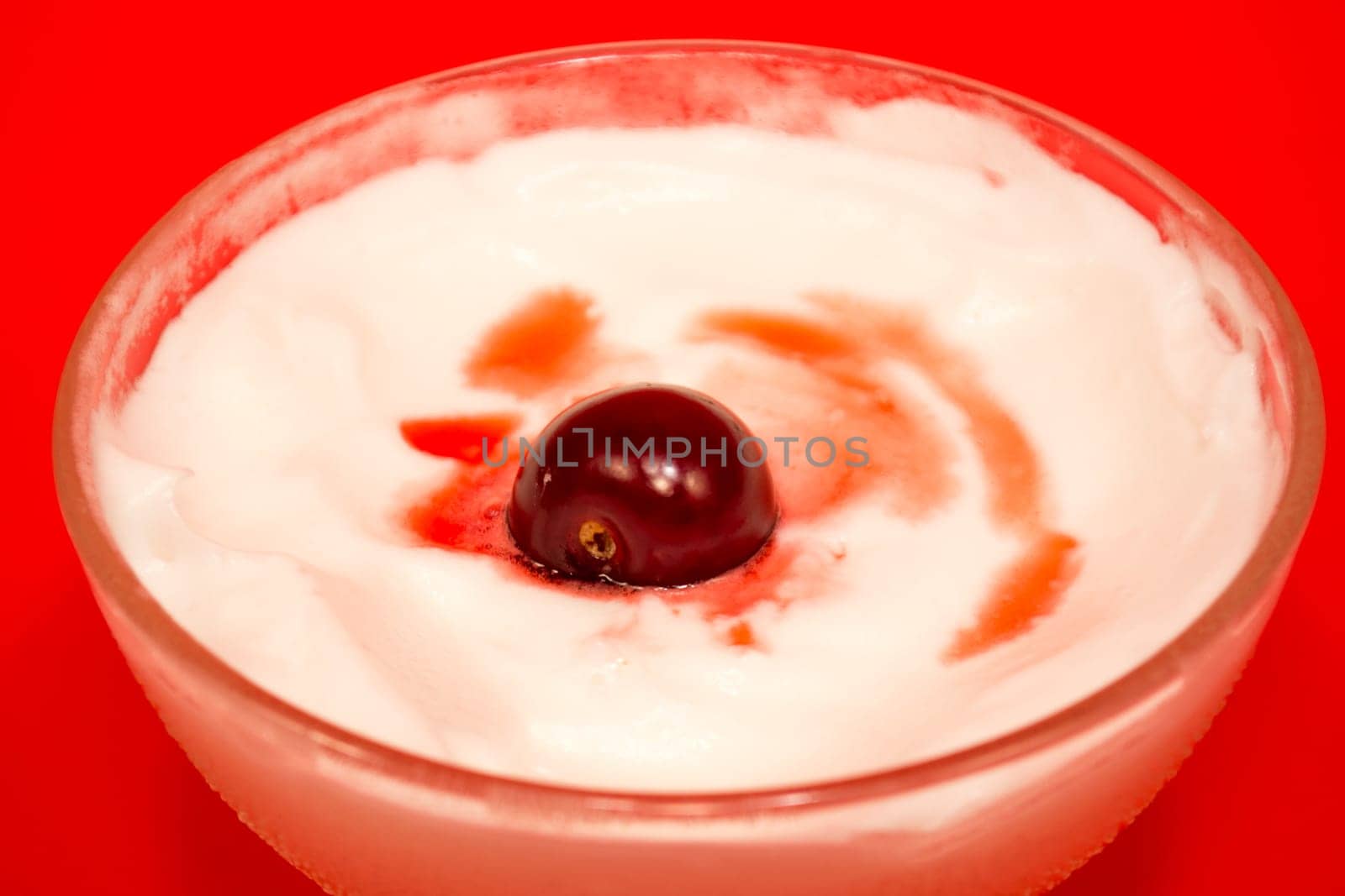 Melted cherry in a cup of vanilla ice cream on red background on red background