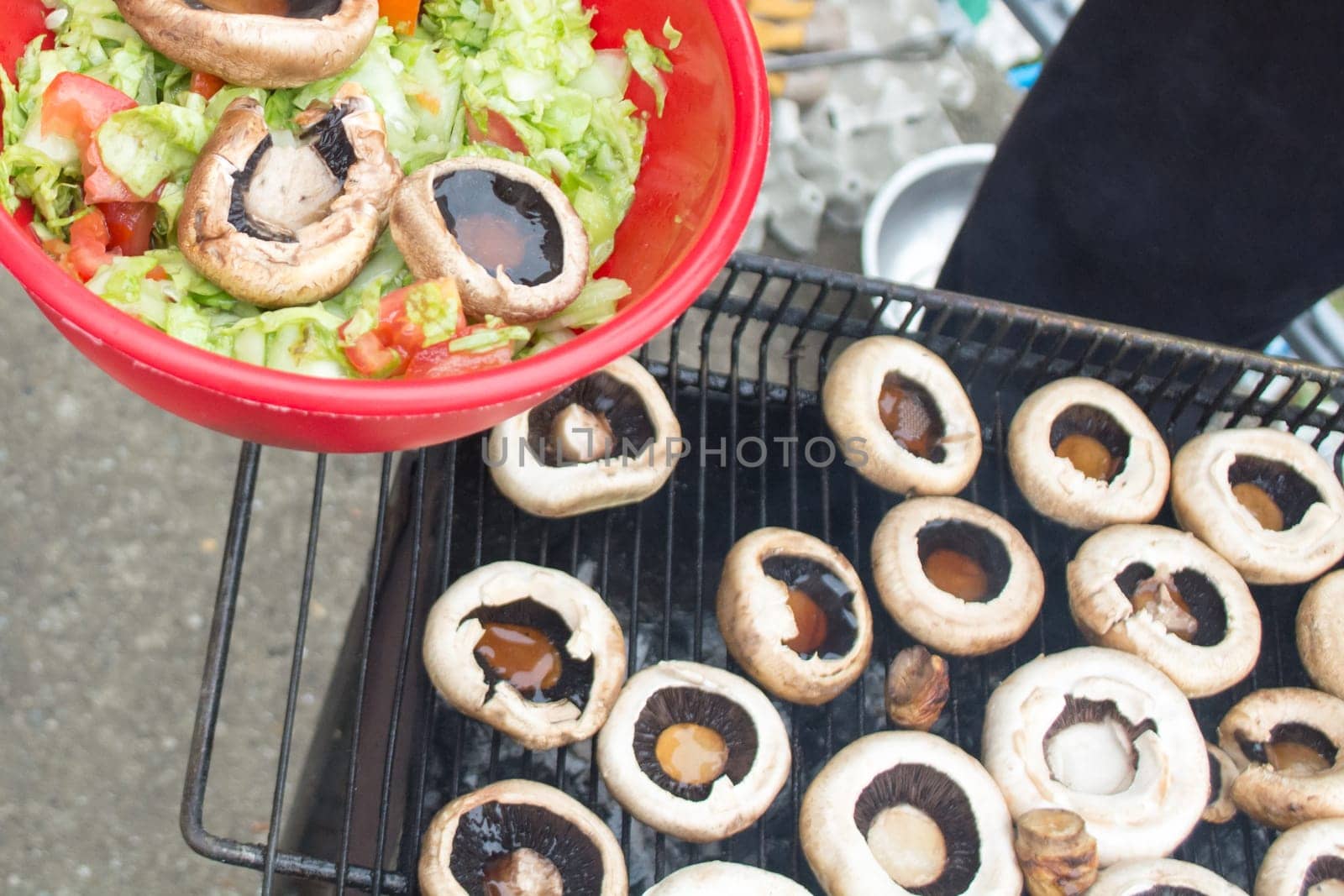 Ball filled up with fresh salad and grilled mushrooms. Barbecue visible in the background