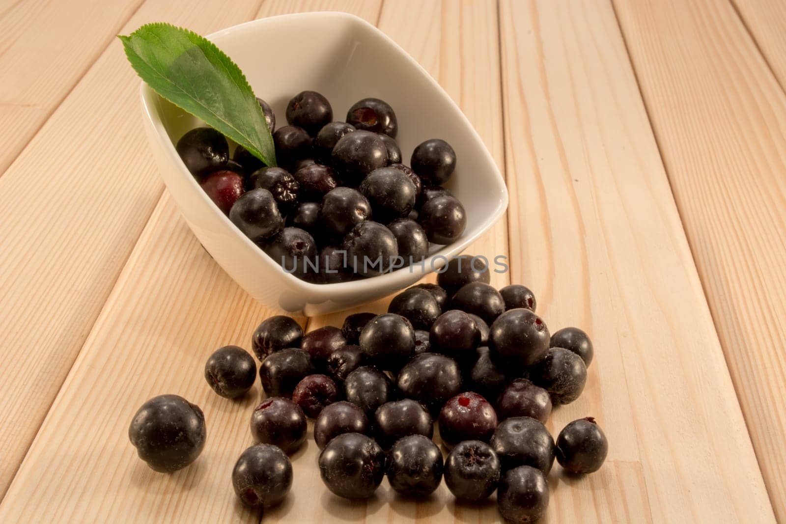 White bowl full with fresh and tasty aronia spilled on wooden table