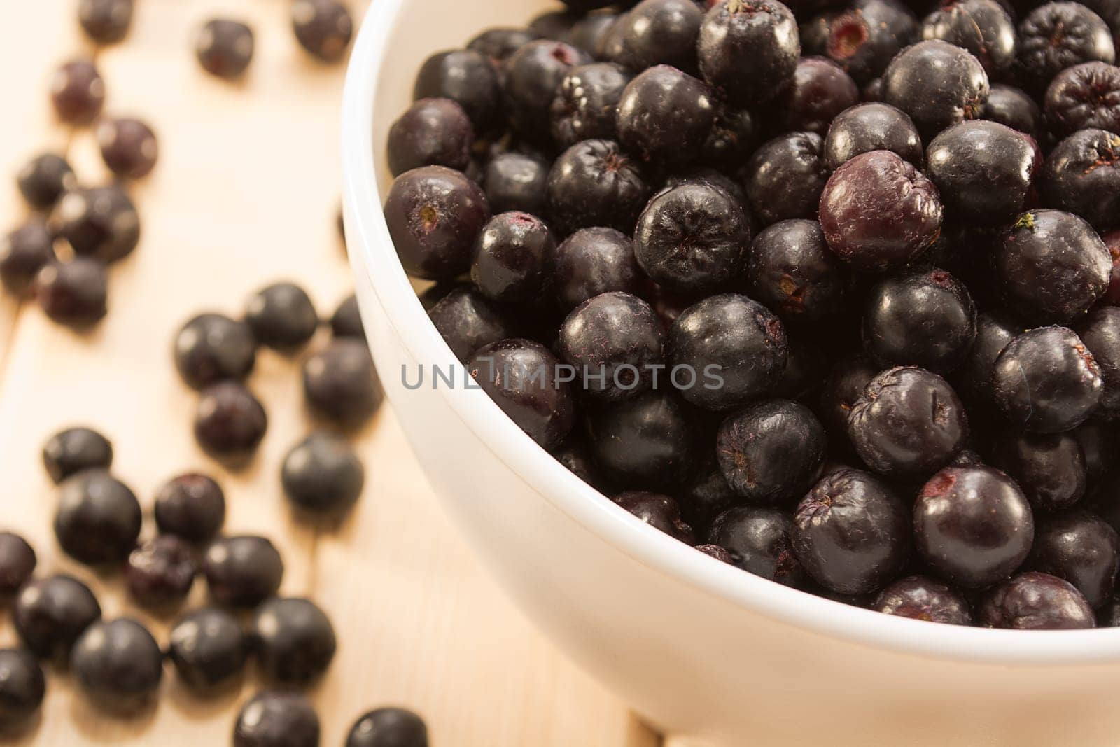 White bowl full with fresh and tasty aronia spilled on wooden table