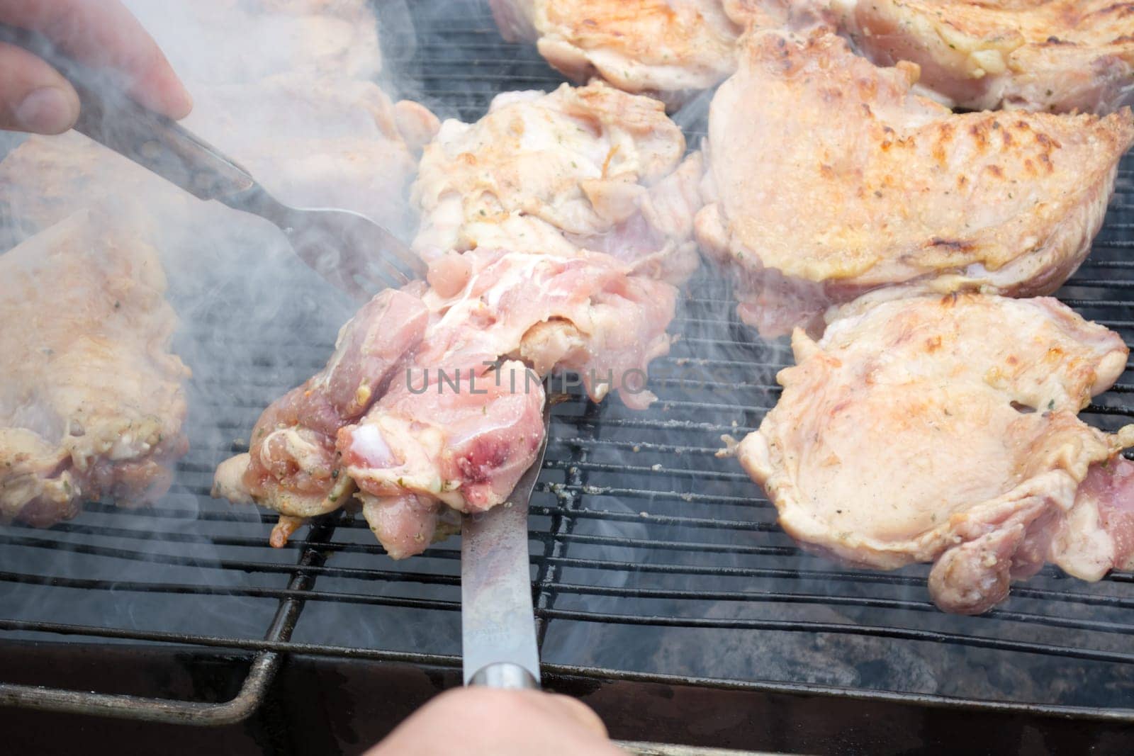 Turning over raw pork chops on grill. Smoke rising from heated grill