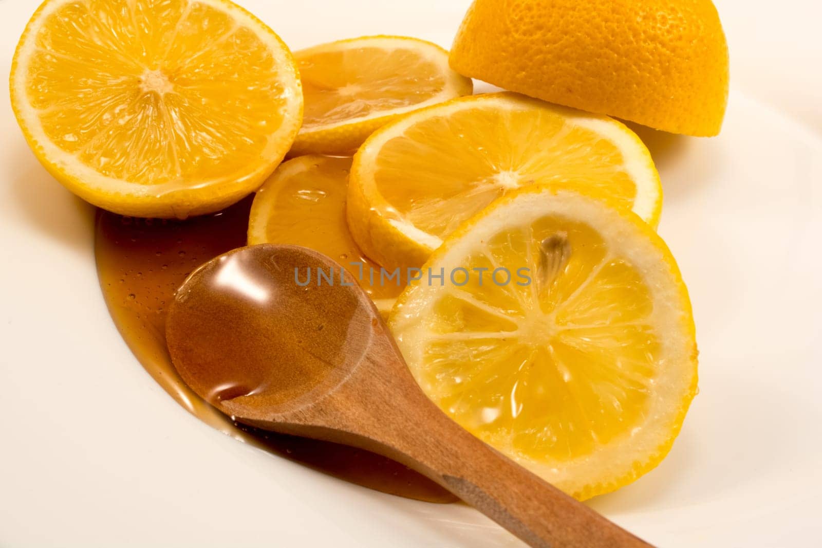 Closeup of sliced lemon and wooden spoon with honey on a plate