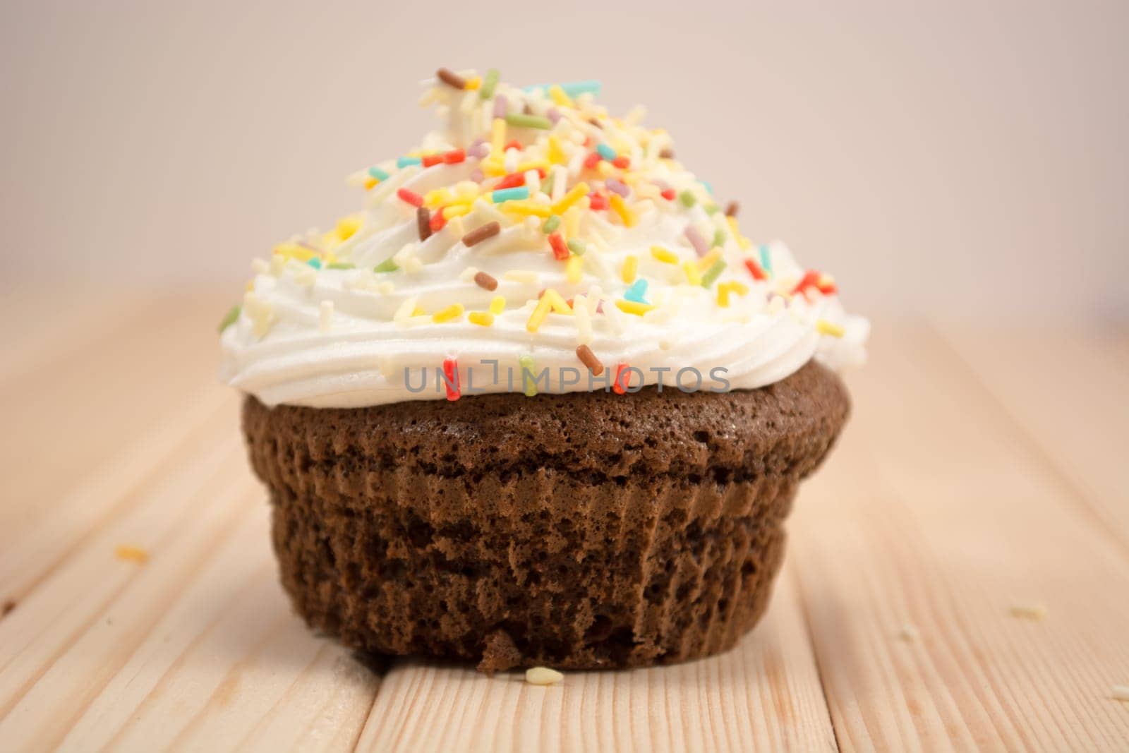 Muffin with cream and colorfull crumbs on top of it sitting on bright wooden table