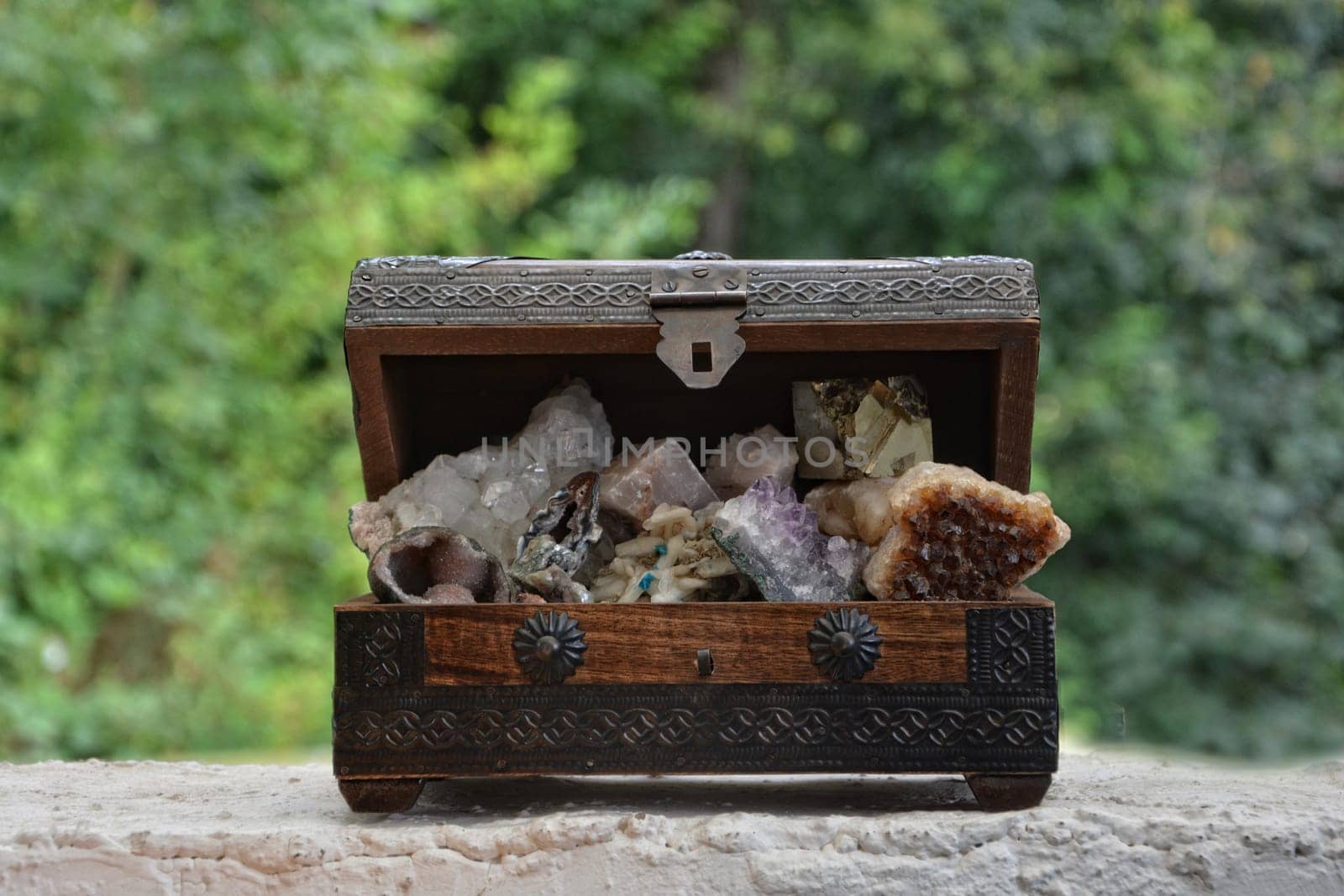 many minerals quartz and crystal stones in wooden box against green nature background