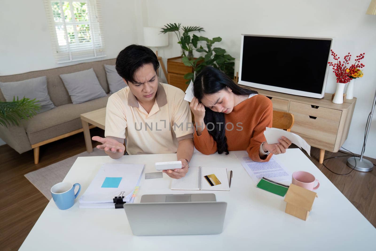 A concerned couple faces financial challenges as they calculate bills and income, expressing frustration and worry together.