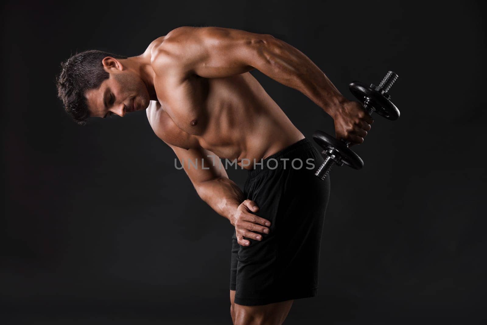 Portrait of a muscular man lifting weights against a dark background
