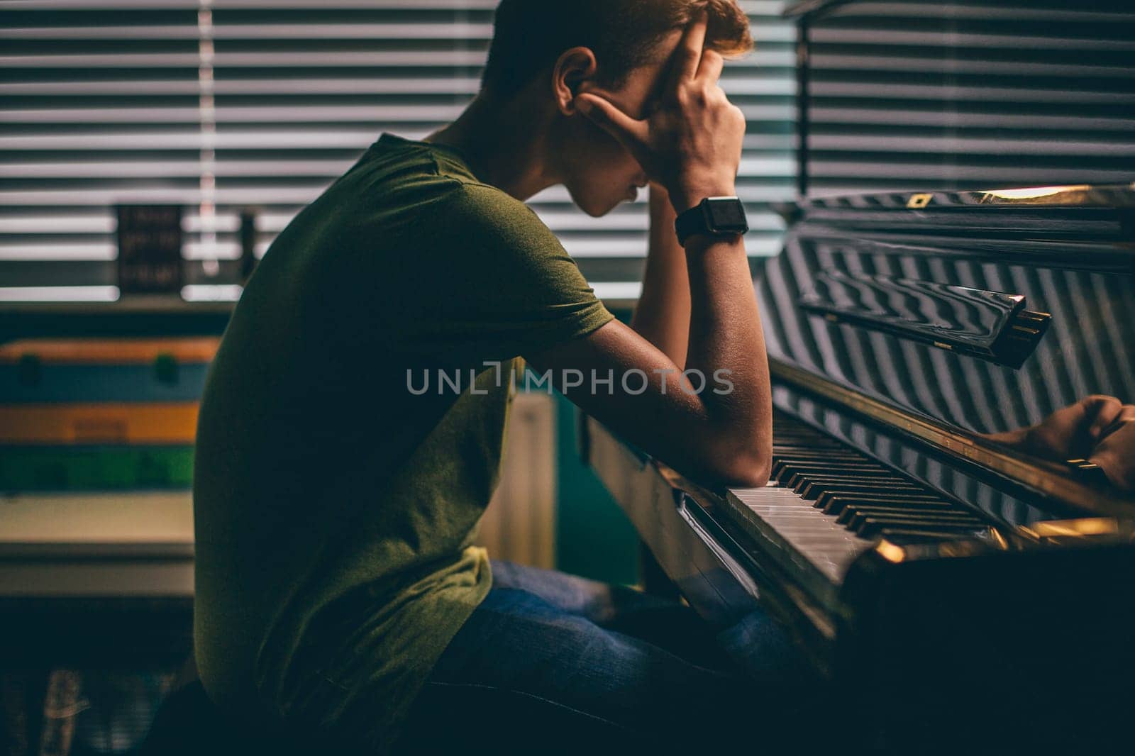Teenager sitting at his piano with his head in his hands.