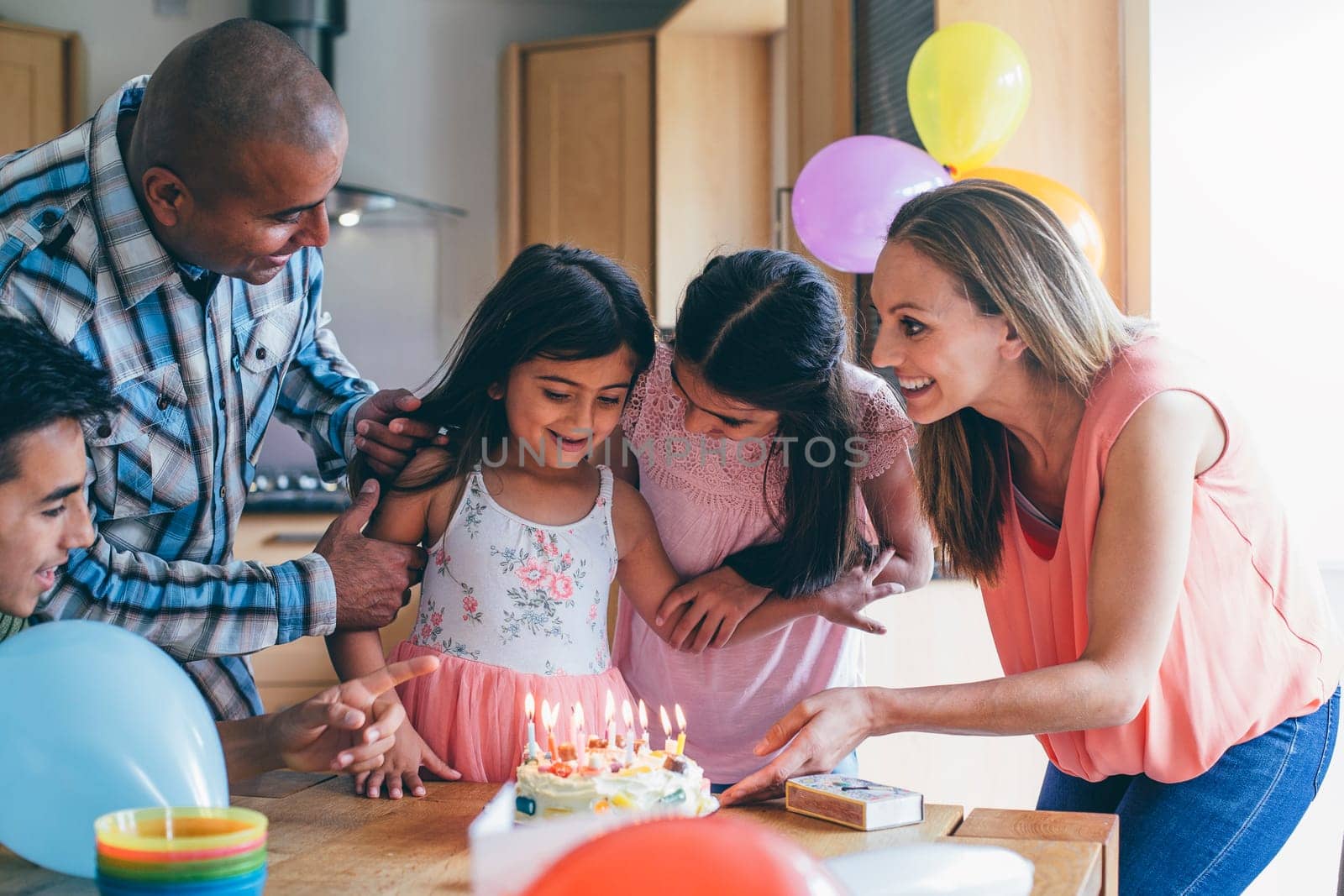 Happy family celebrating the youngest girls birthday with cake at home. They are singing to her before she blows out the candles.