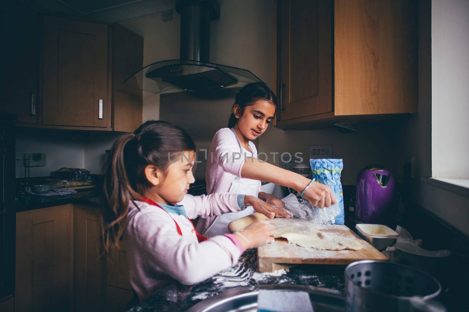 Sisters preparing dough to make biscuits in the kitchen of their home.