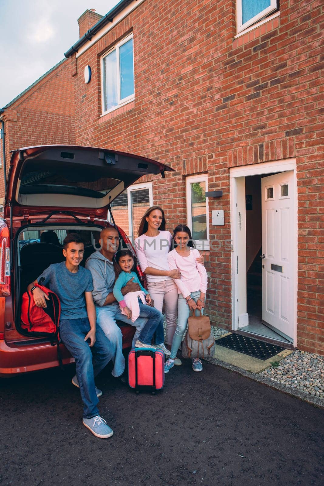 Happy family posing with their car outside of their home before their journey.