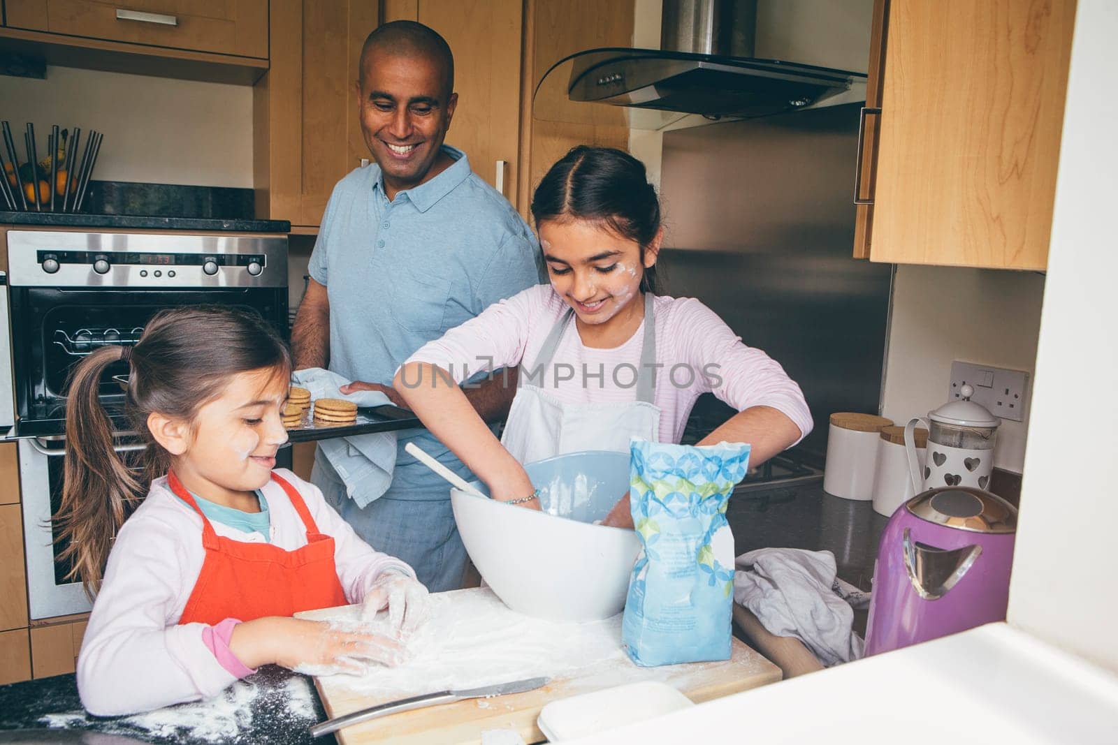 Father making biscuits with his two daughters in the kitchen of their home.