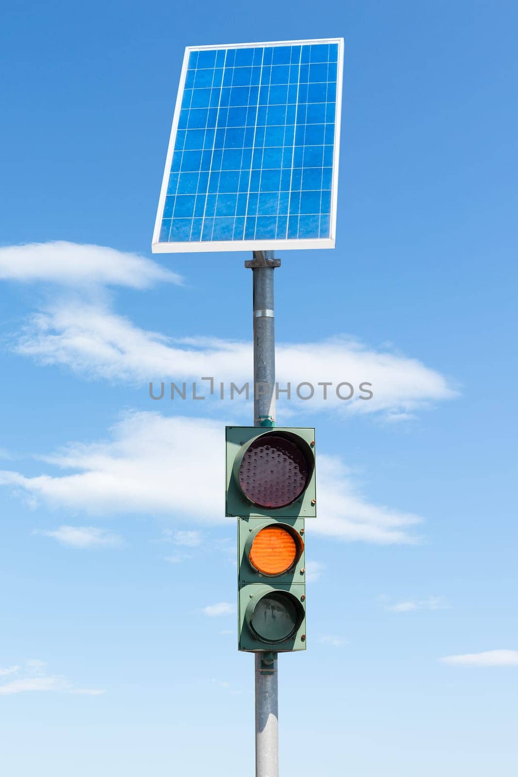 Road traffic light powered by electricity generated from a solar panel. Blue sky