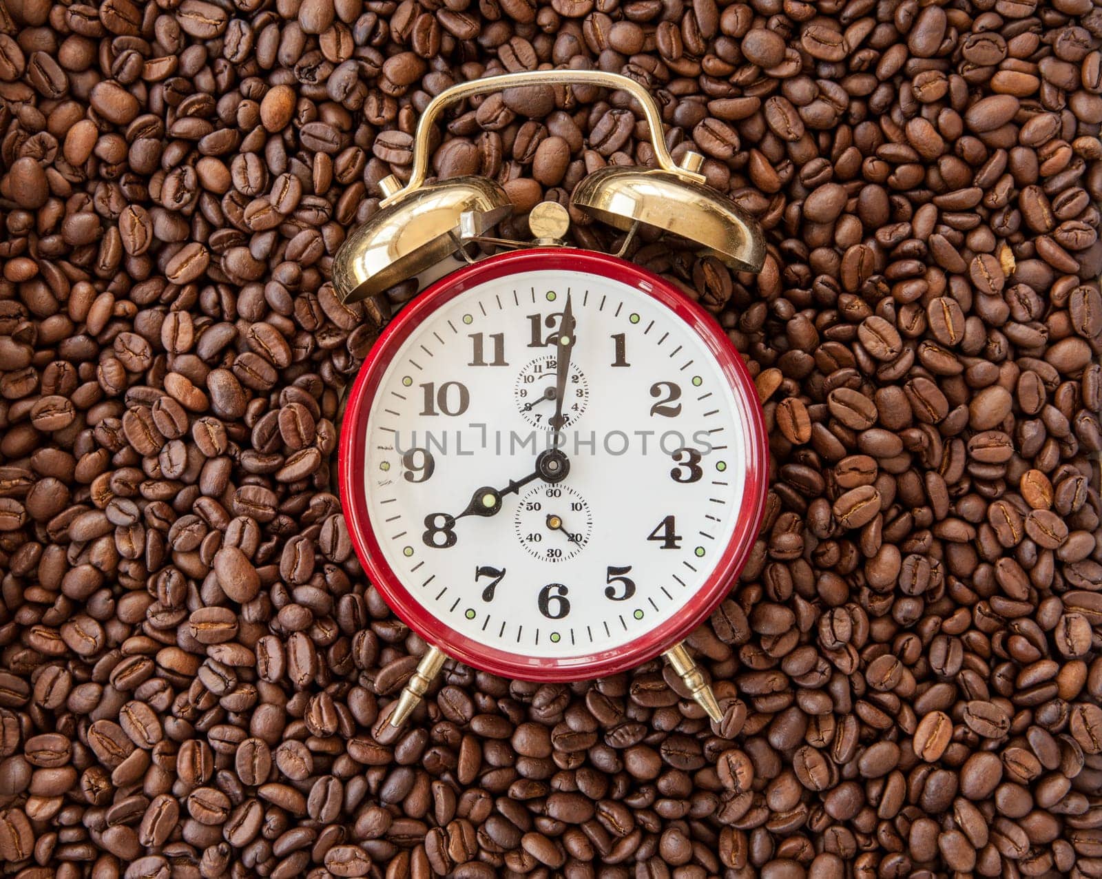 Vintage alarm clock shows 8 o'clock on background of coffee beans