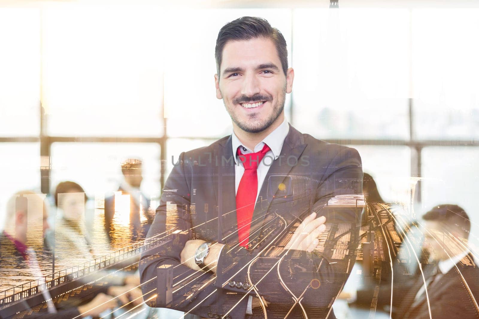 Successful team leader and business owner proudly standing with crossed arms with coworkers working in office in background. City reflection in window. Business and entrepreneurship concept.