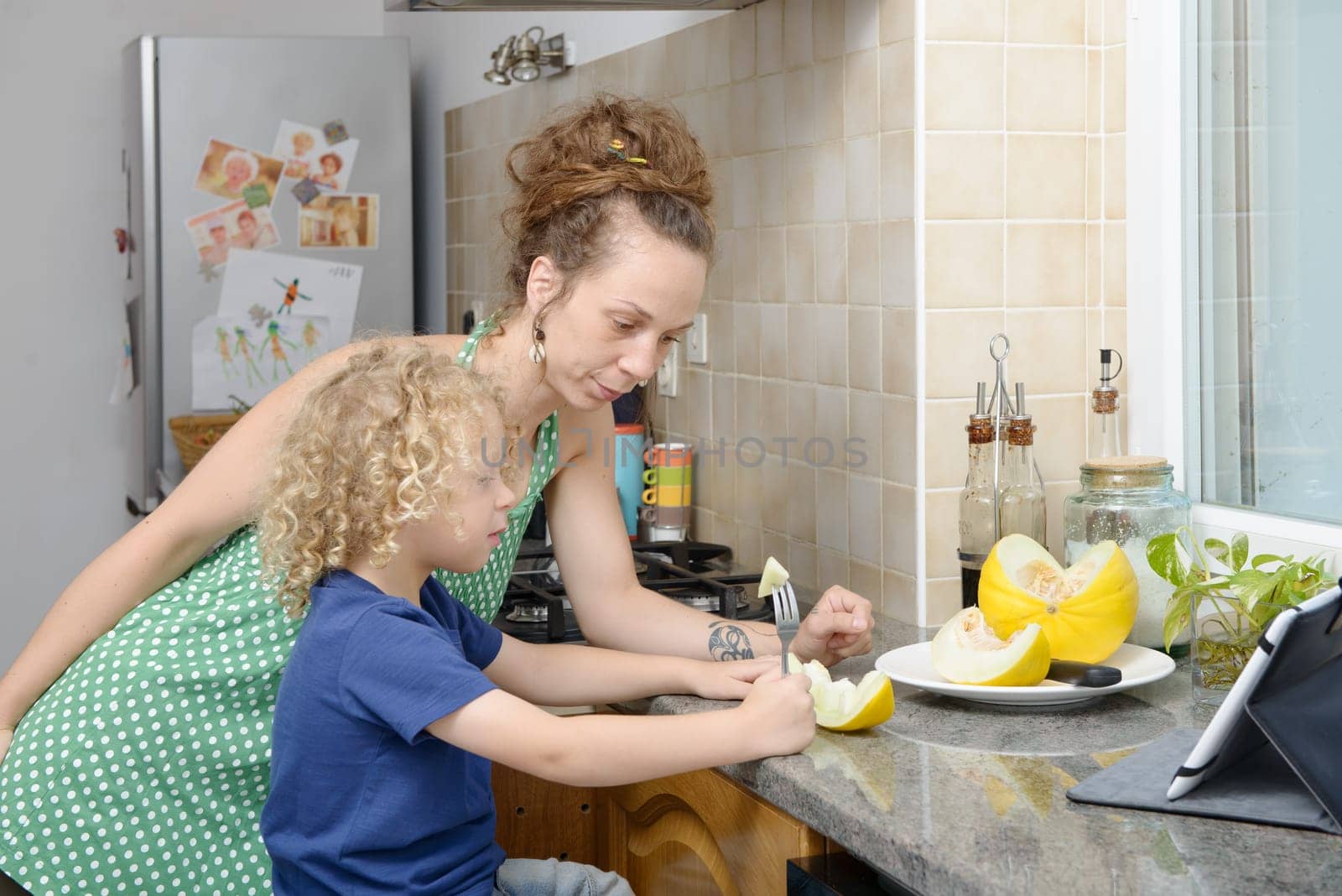 a child and his mom with a melon in kitchen