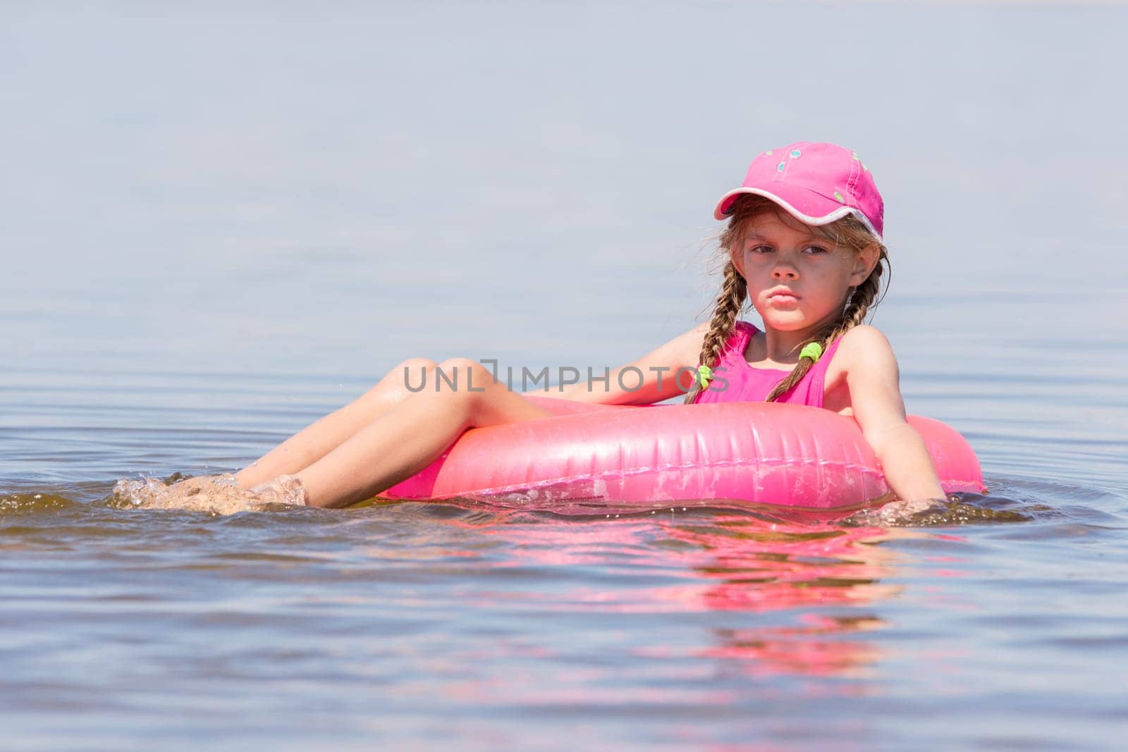 Sad girl in a cap floating in the river sat on the swimming circle