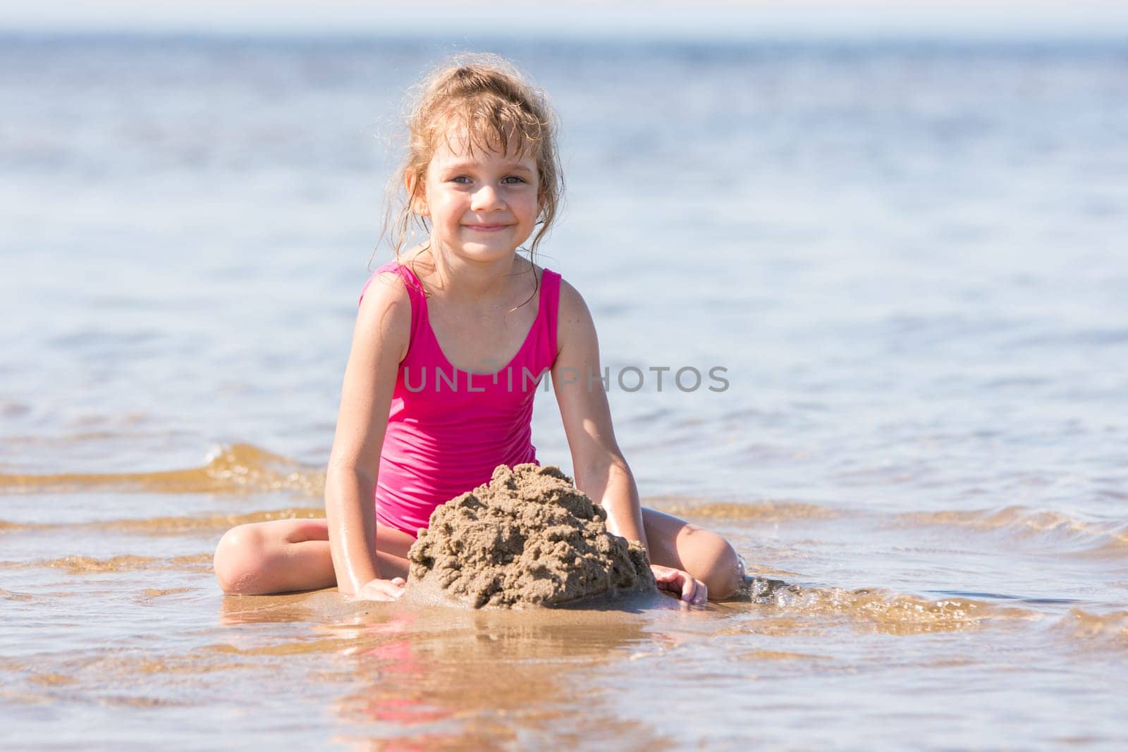 Five-year girl in a pink bathing suit playing in the sand in the shallows of the river