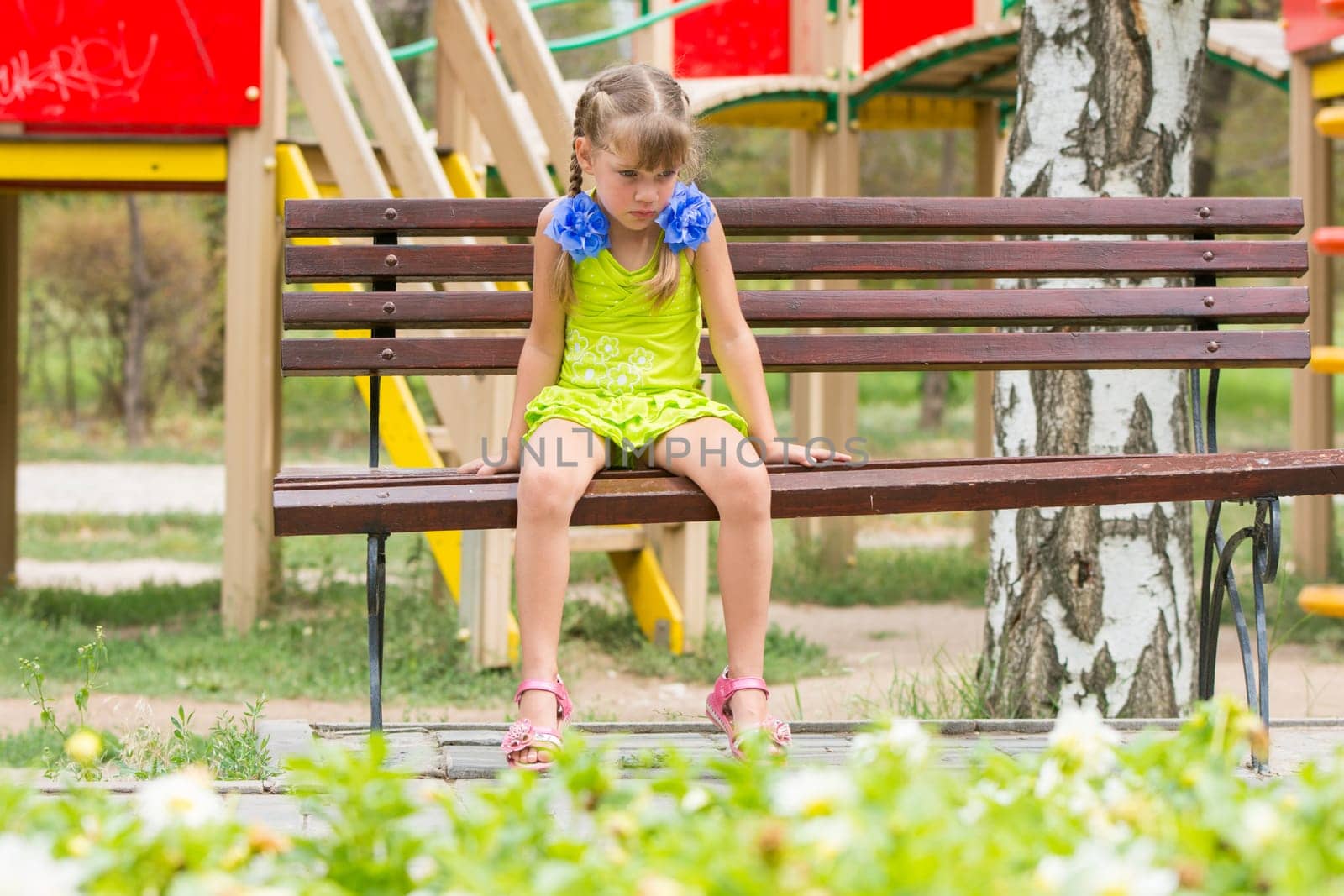 Crying girl sitting on the bench on the background of the playground
