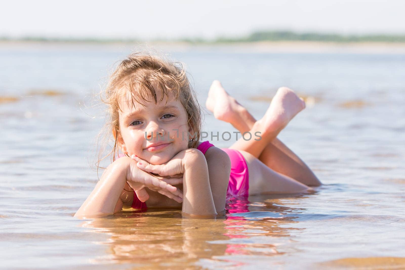 Five-year girl lies in water in the shallows of the river