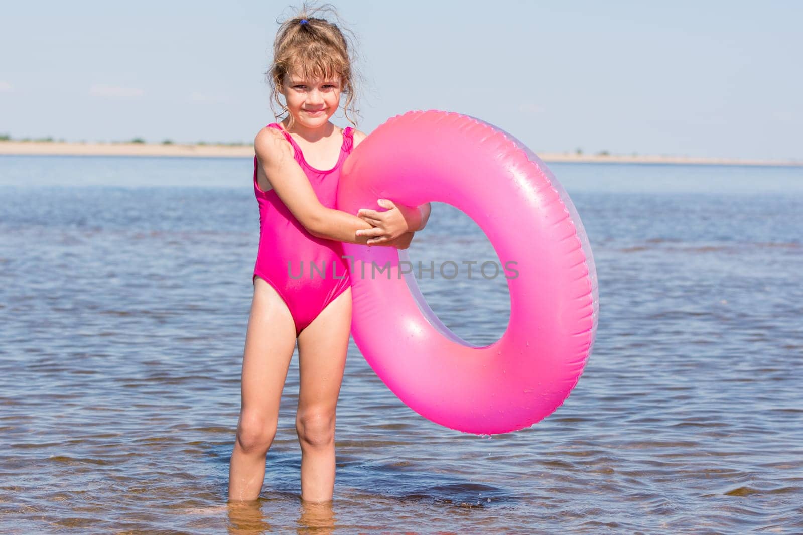 Five-year girl in a pink bathing suit standing with swimming laps in the river
