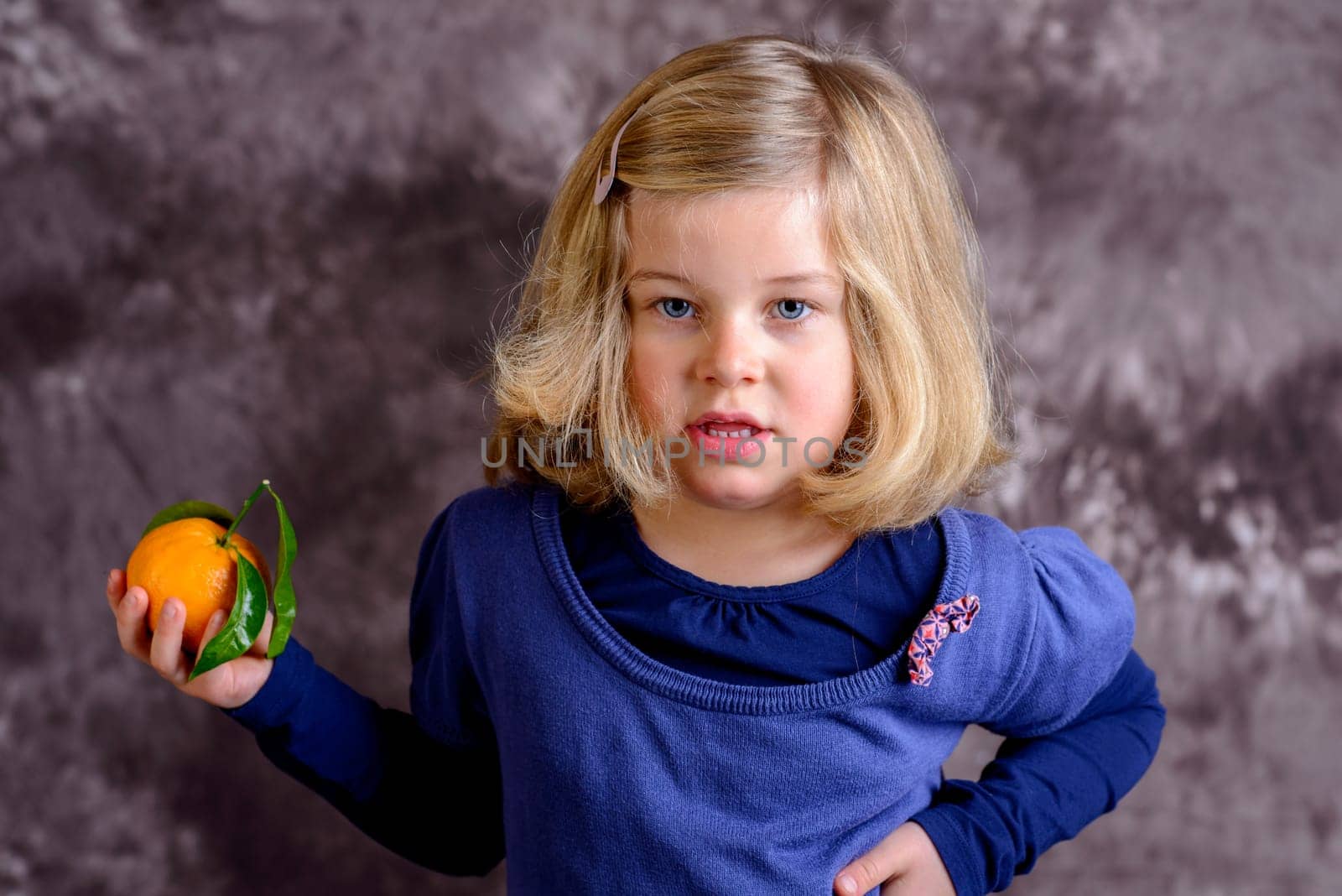 little girl with mandarin orange in front of brown background