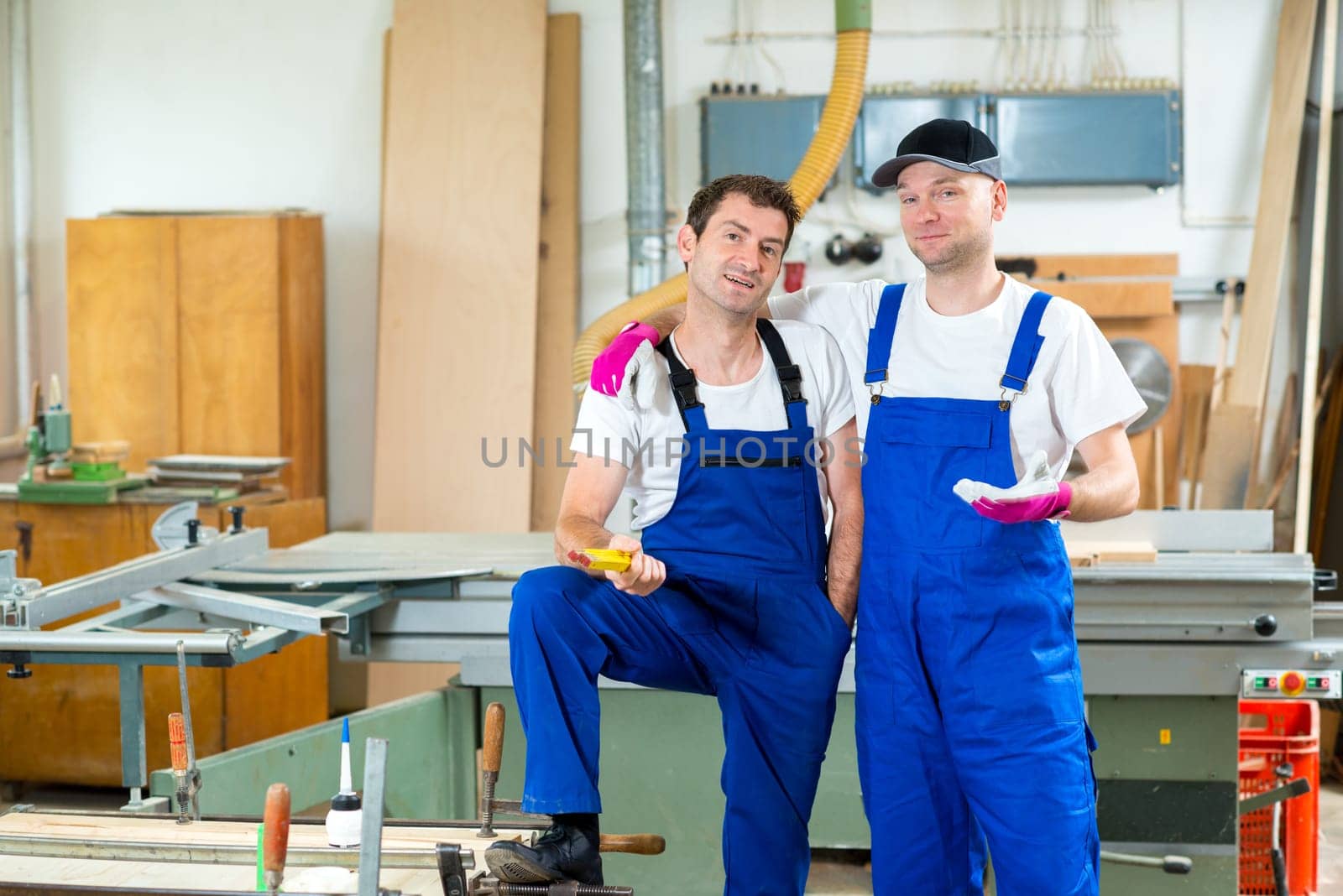 two worker in blue dungarees in a carpenter's workshop