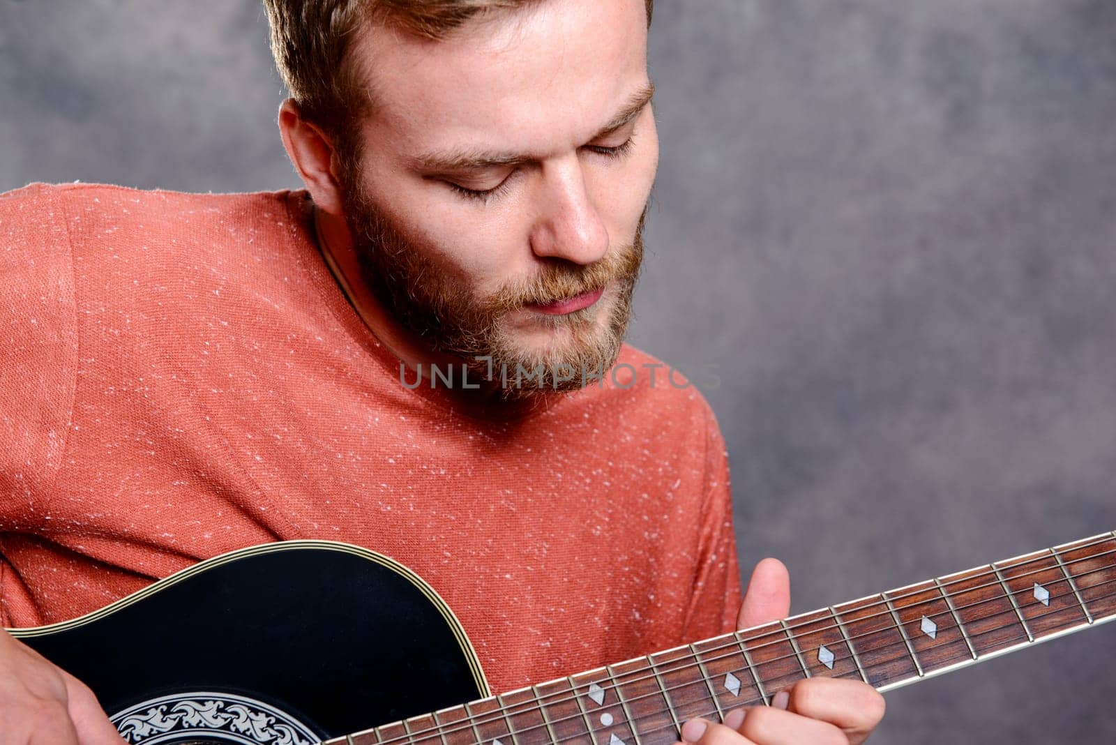 young bearded man in red shirt playing acoustic guitar
