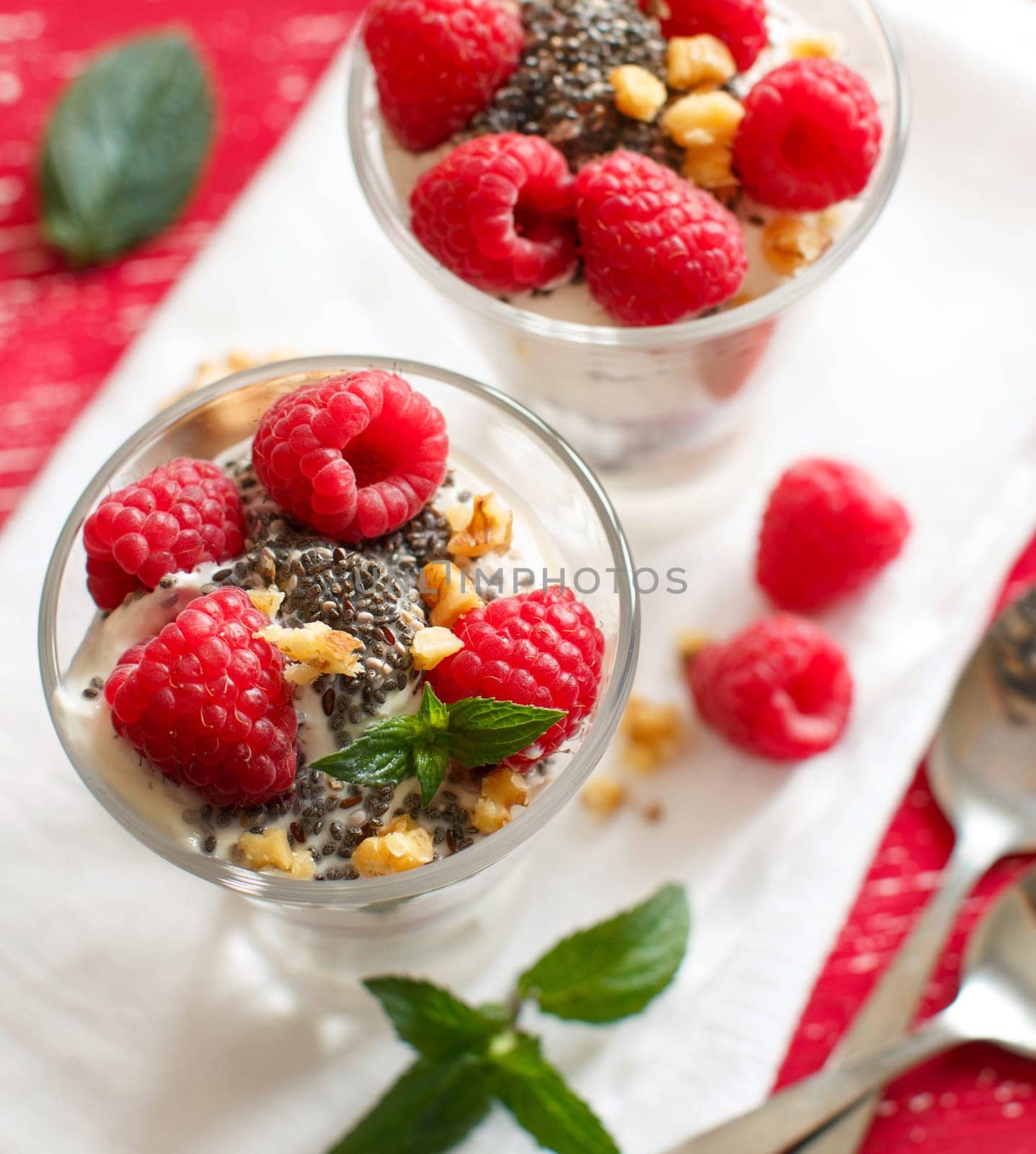 Yogurt with chia seeds, walnuts, mint and raspberries on red background