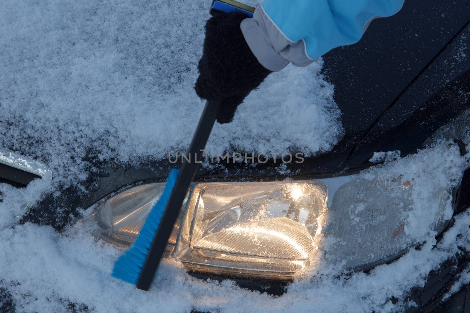 Snow covered car lights being cleared off