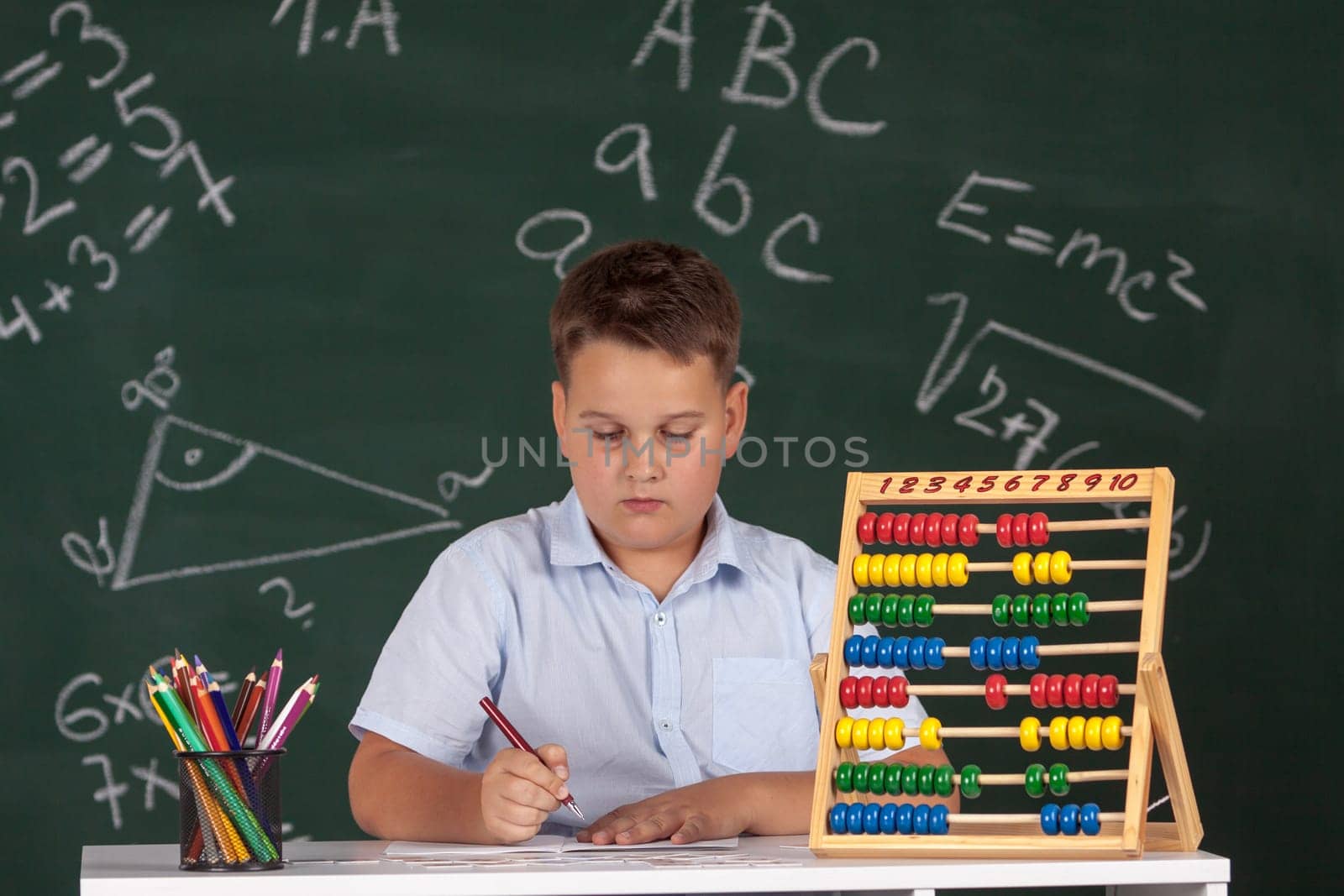 Young boy described at the green blackboard at school thinking about the task