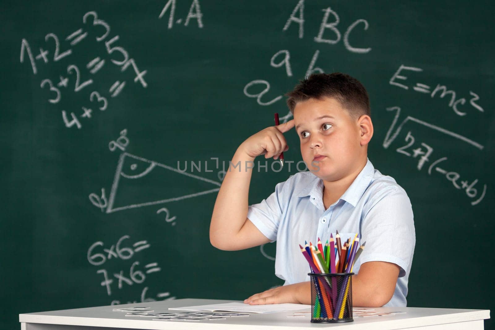 Young boy described at the green blackboard at school thinking about the task