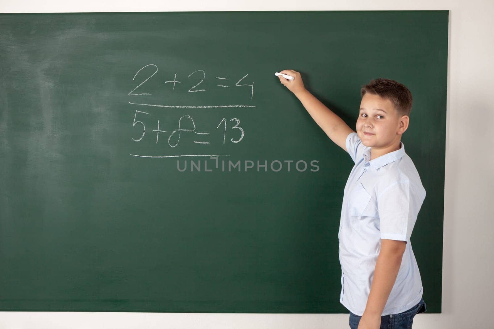 Young boy writing mathematical examples on the a school blackboard