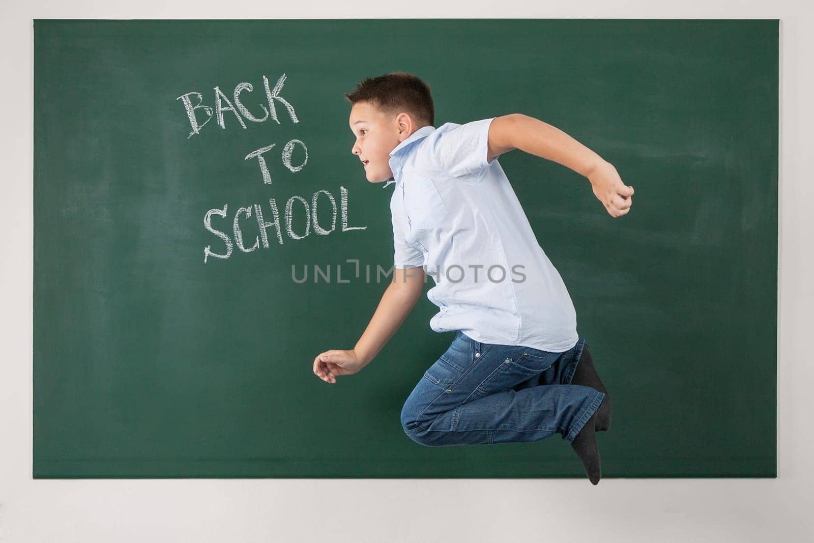 Young boy jumping in a green chalkboard with the words back to school