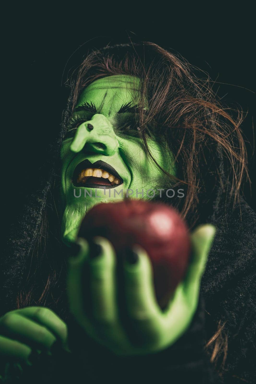 Green witch laughing while holding an apple in her hand. Shallow depth of field.