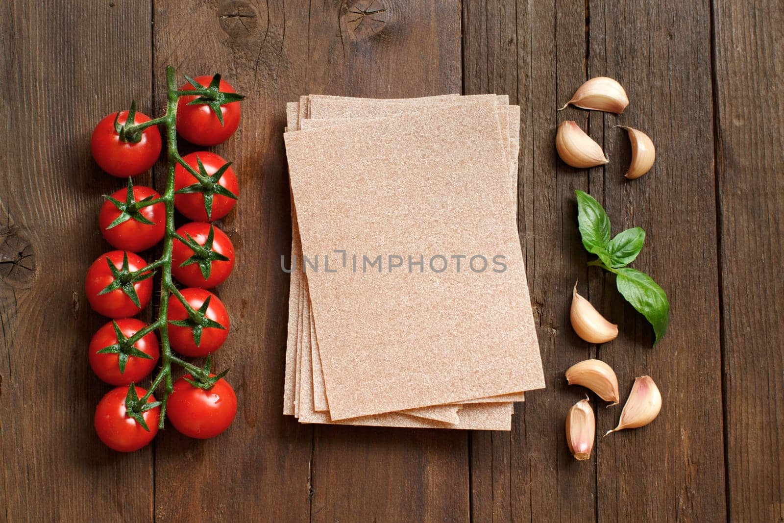 Whole wheat lasagna sheets, tomatoes, garlic and basil on wooden background