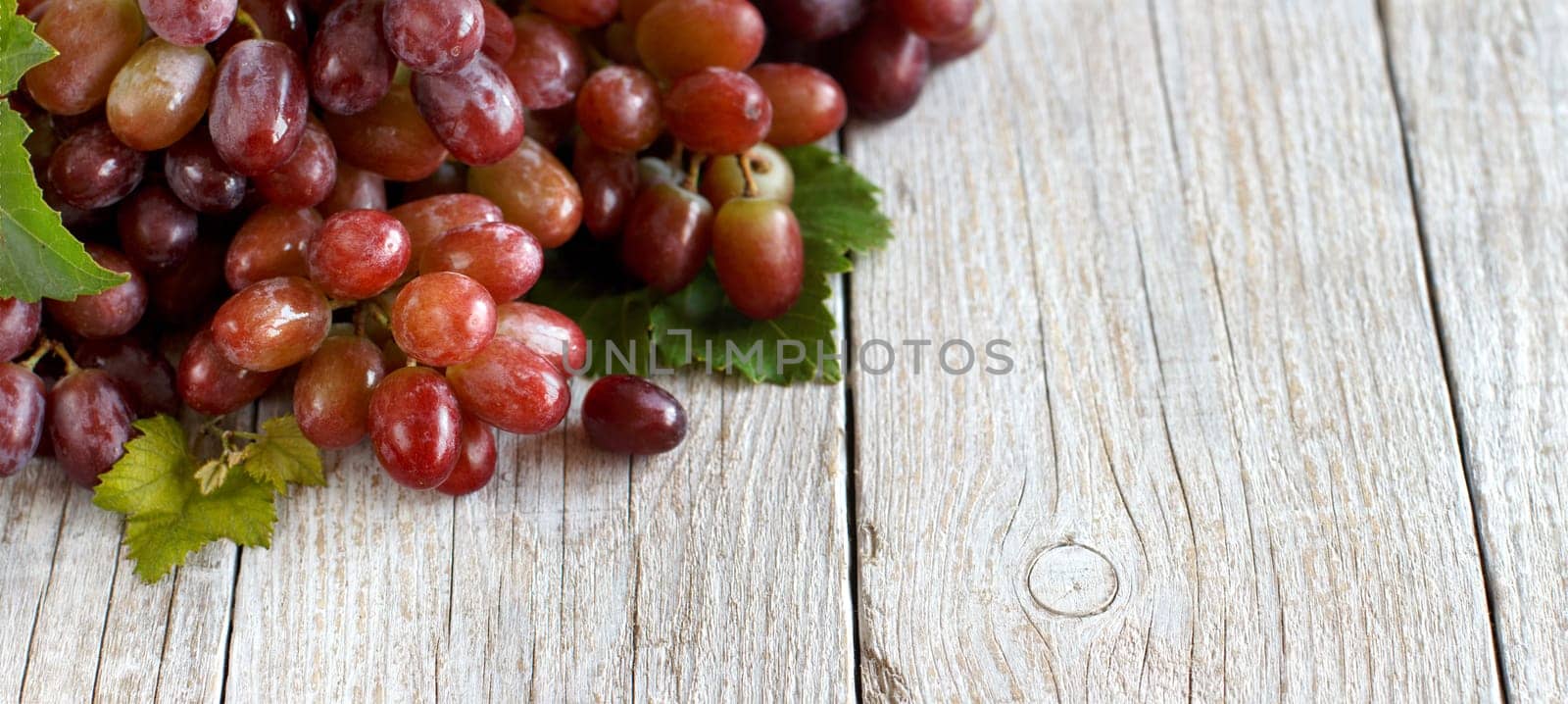 Red grapes with leaves on a old wooden table close up