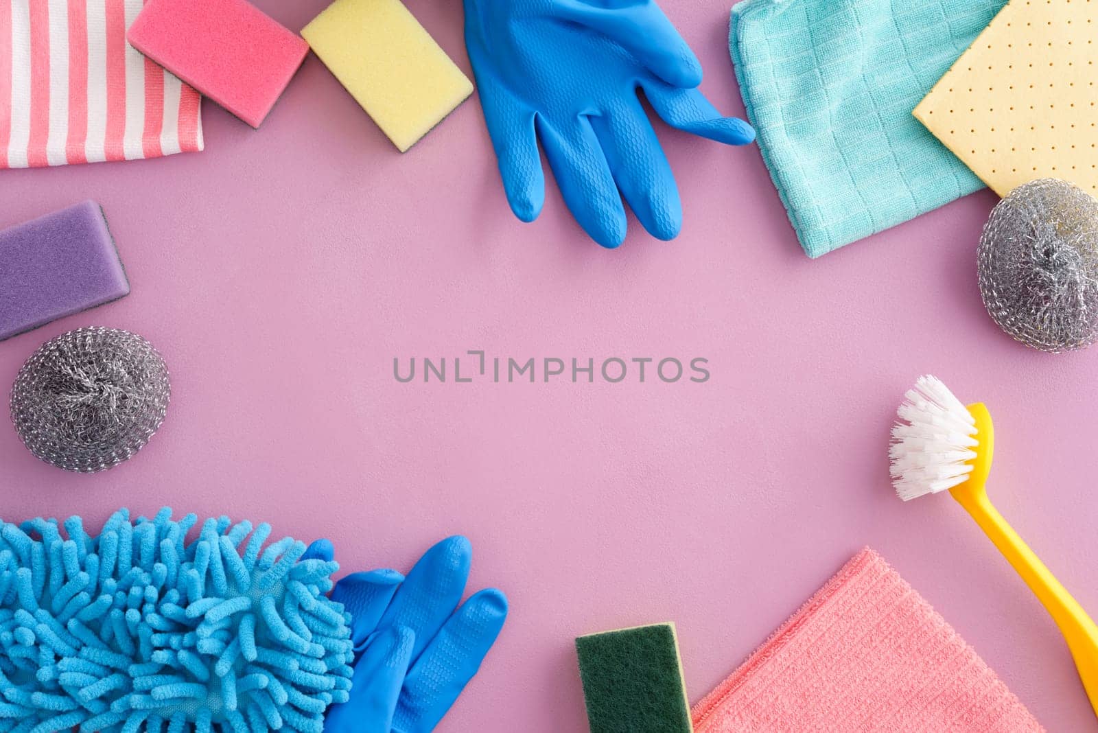 Collection of pastel-coloured cleaning supplies on pink background with copyspace