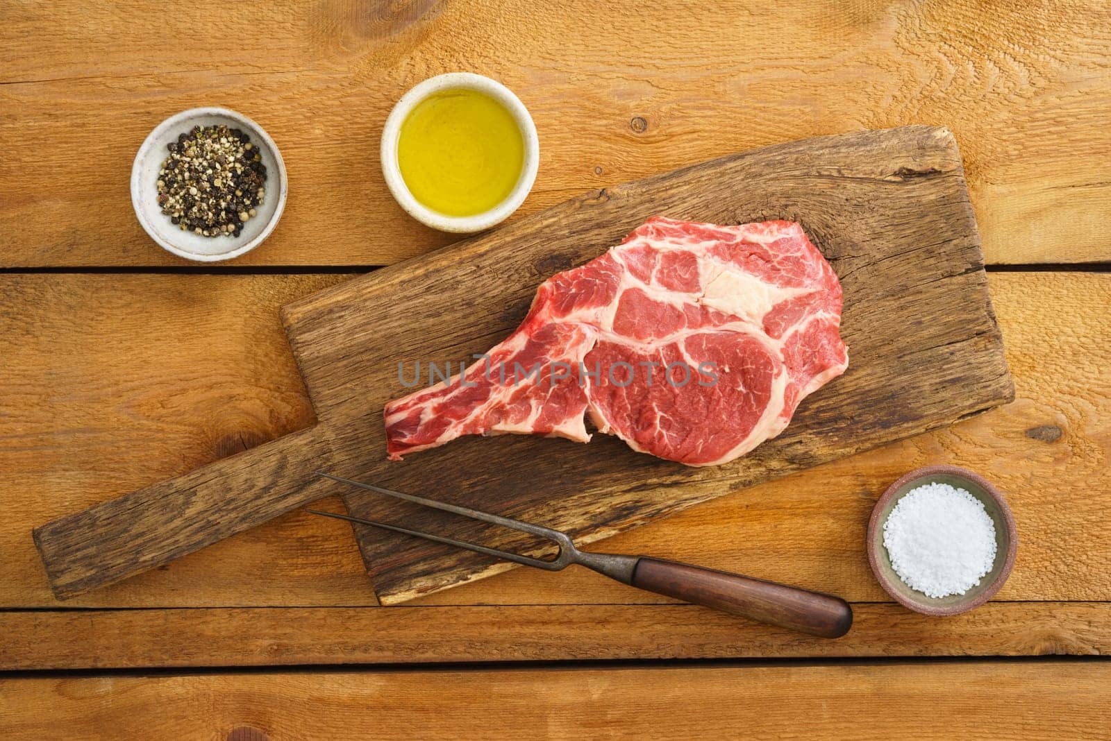 Dry aged Rib eye steak on wooden board with pepper, salt and oil