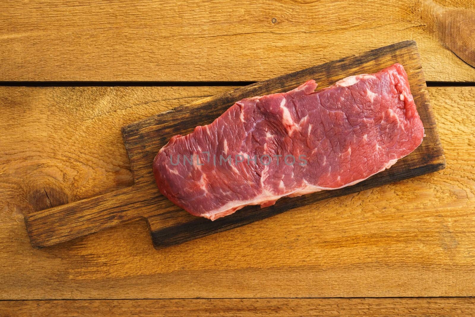 Uncooked rump steak on wooden board on wood