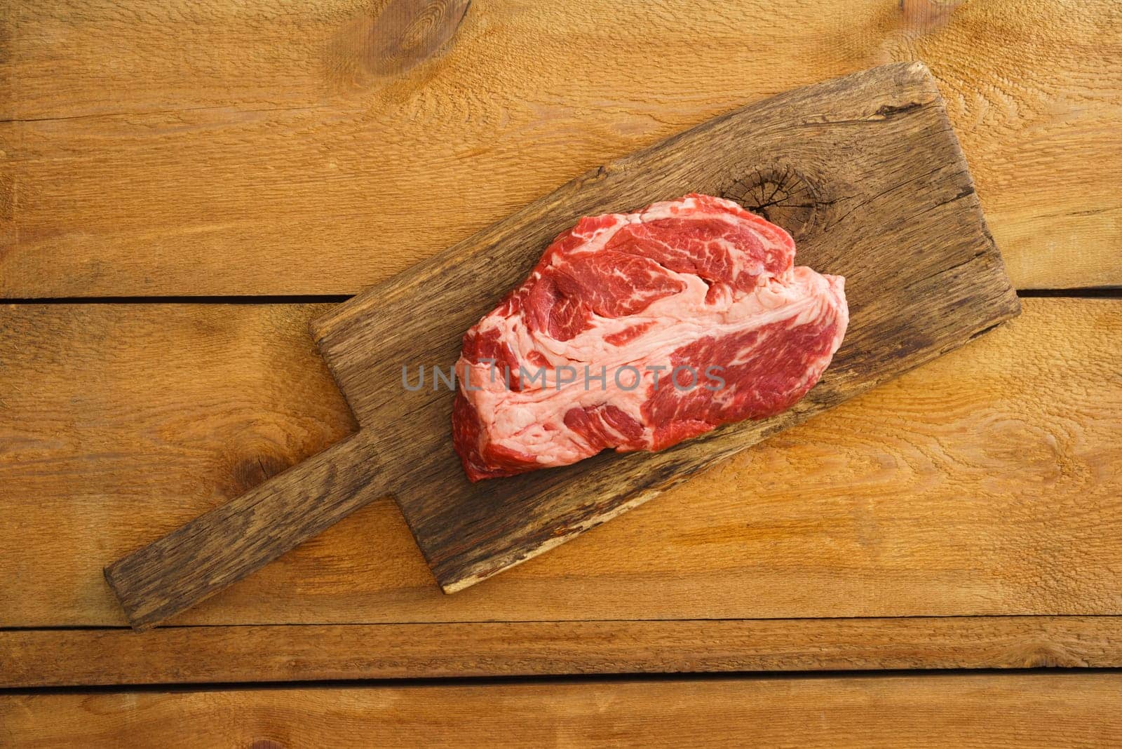 Uncooked chuck eye steak on wooden board