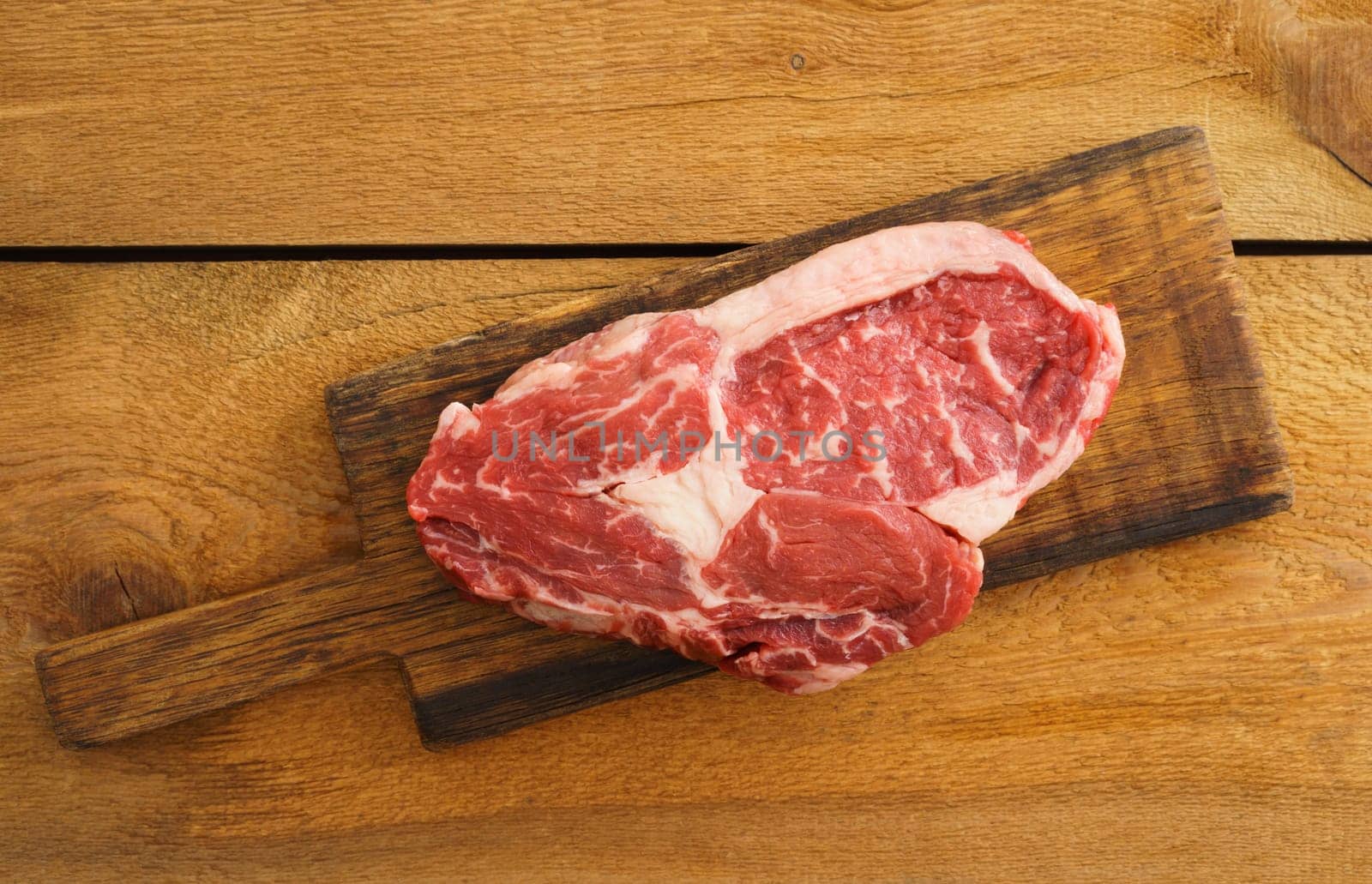 Uncooked rib eye steak on wooden board