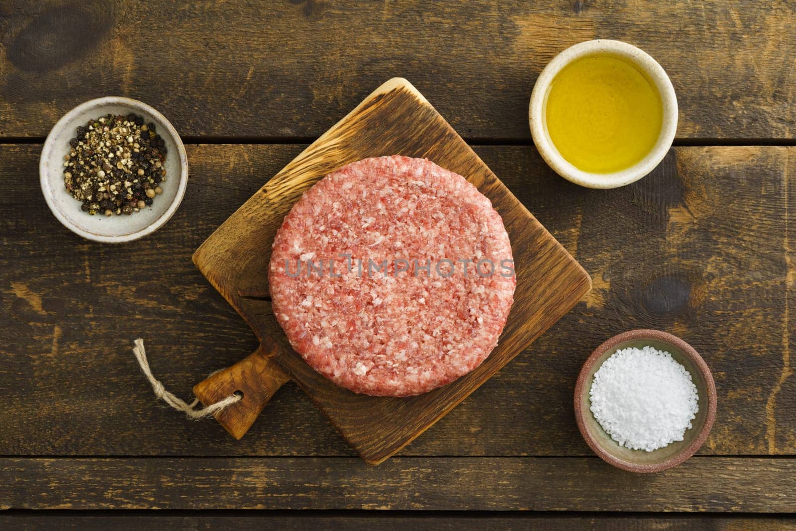 Burger patty from ground beef on wooden board with olive oil, salt and pepper